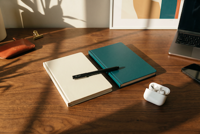 Zwei hochwertige Notizbücher cream und deep teal nebeneinander mit AirPods — zwei Sparring-Sessions